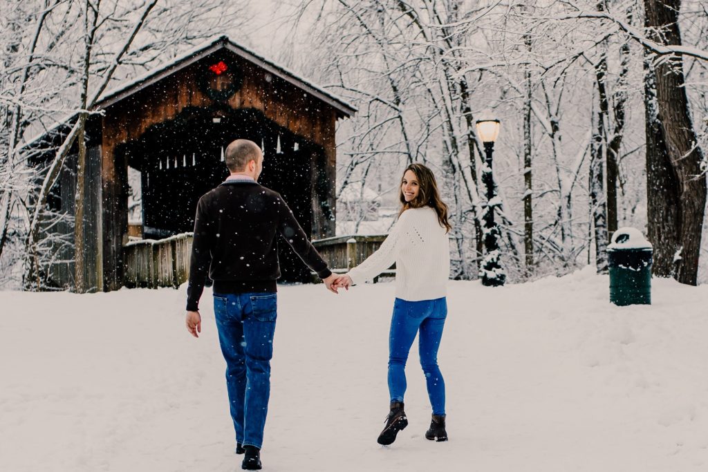 couple walking towards covered bridge in the snow
